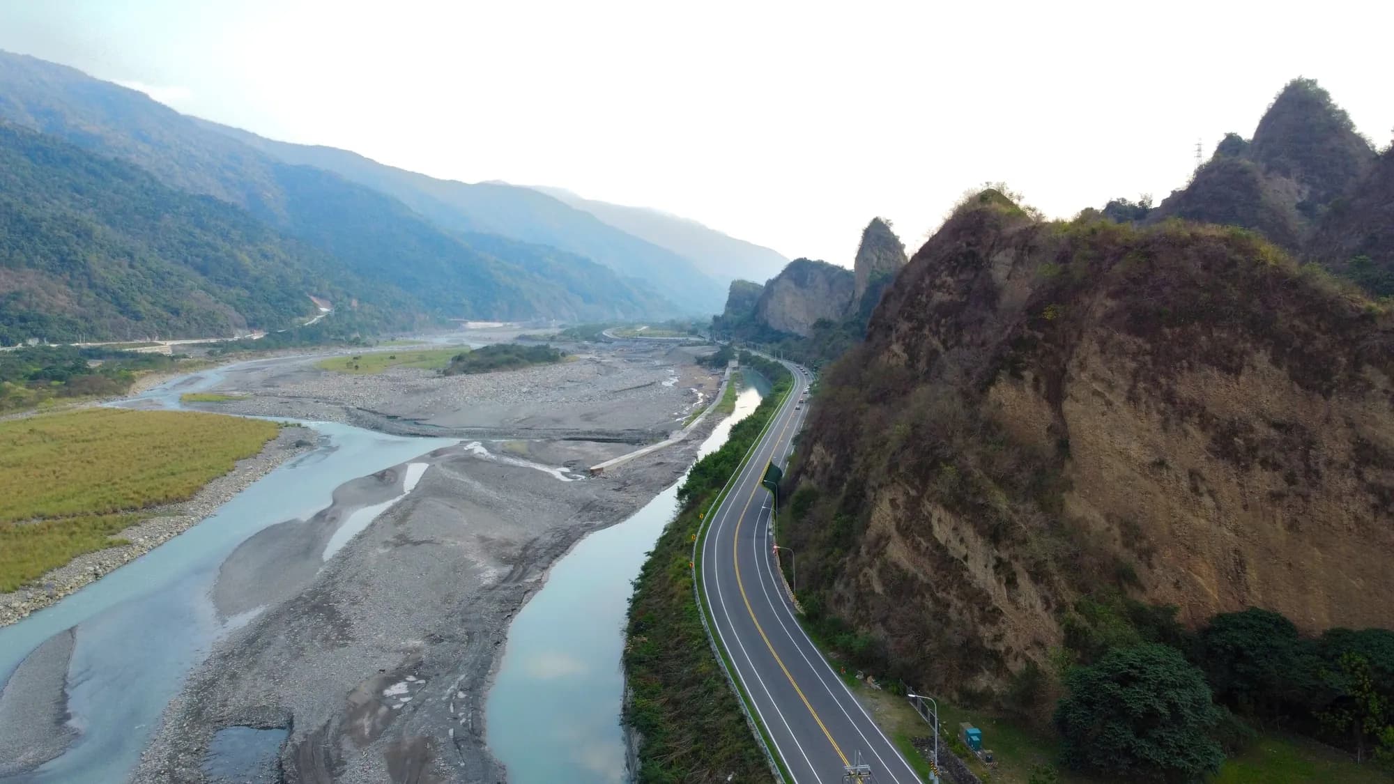 Forested mountains above a river valley, with a road along the bank